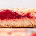 Side view of a strawberry crumble bar slice resting on a spatula, showing every layer.