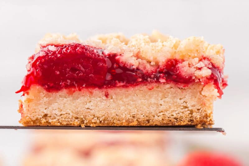 Side view of a strawberry crumble bar slice resting on a spatula, showing every layer.