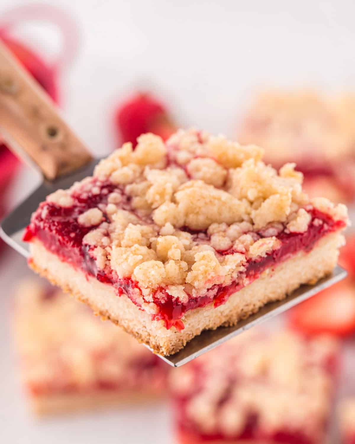 Spatula holding up a strawberry bar with shortbread crust and crumb topping.