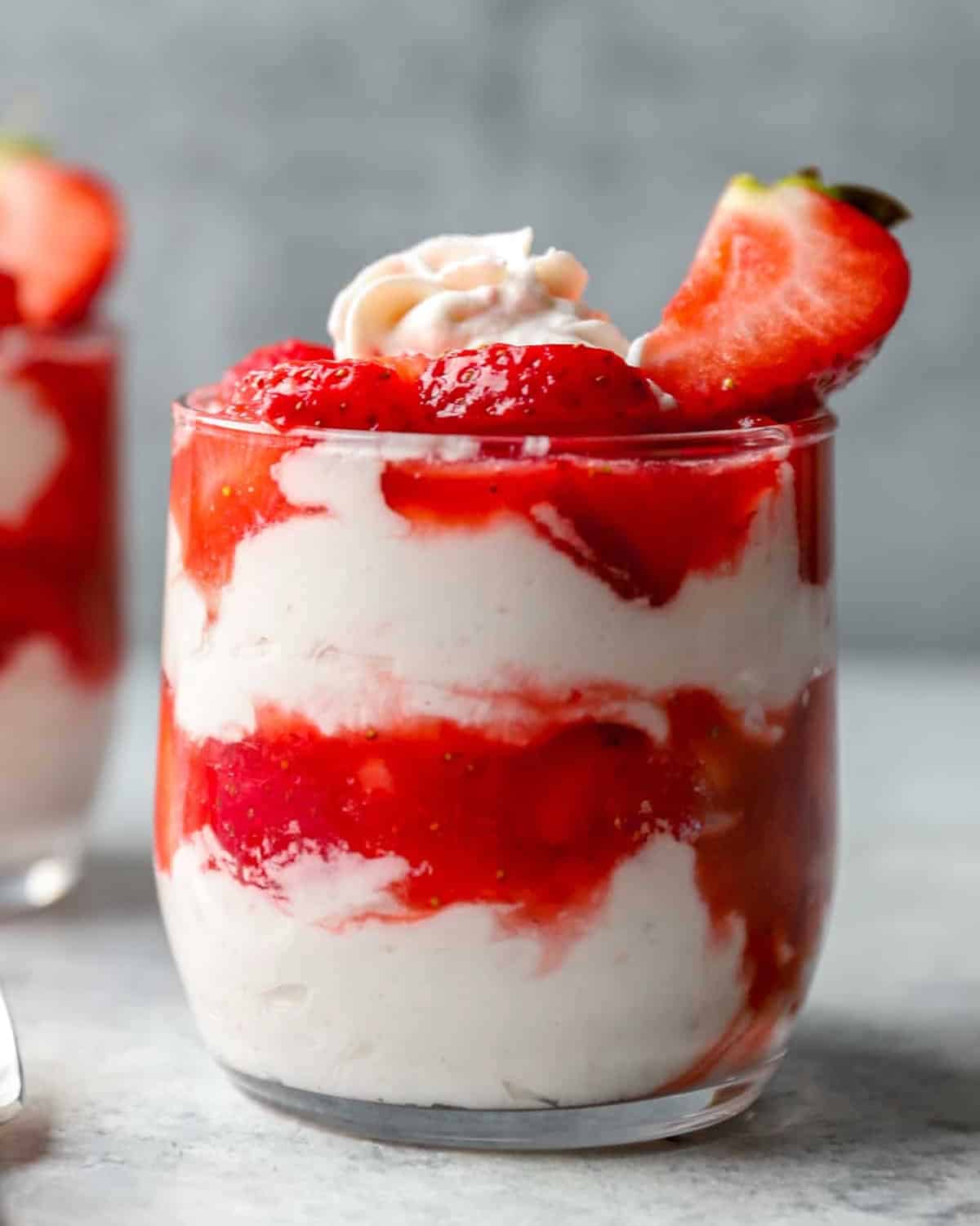 A strawberry fool in a glass, showing layers of whipped cream and pureed berries.