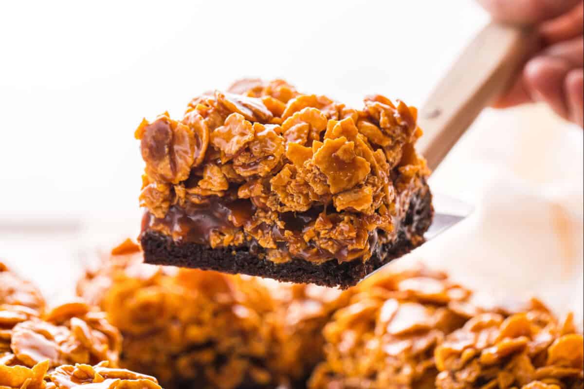 A spatula lifting a caramel cornflake brownie with layers of fudgy brownie, sweet caramel, and crunchy cornflakes.