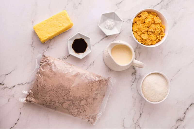 Ingredients for caramel cornflake brownies, featuring boxed brownie mix, granulated sugar, heavy whipping cream, unsalted butter, cornflakes, vanilla, and salt.