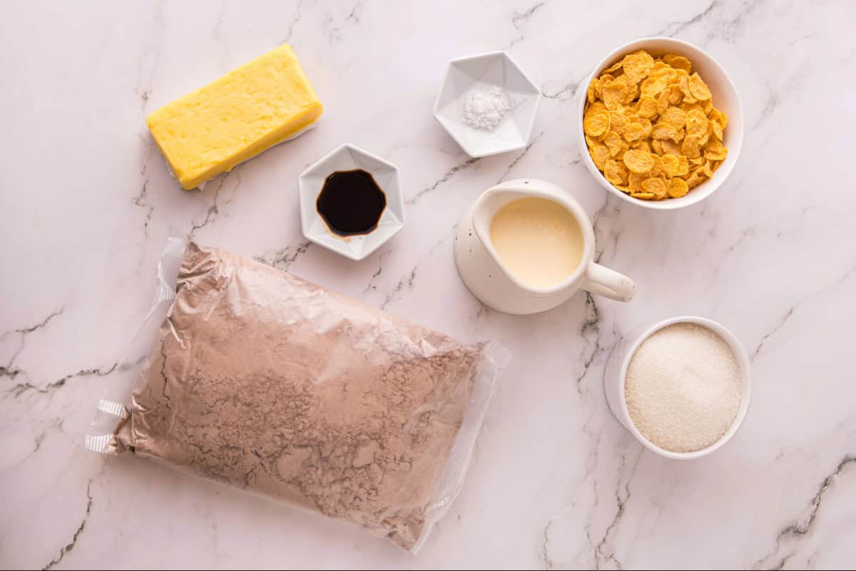 Ingredients for caramel cornflake brownies, featuring boxed brownie mix, granulated sugar, heavy whipping cream, unsalted butter, cornflakes, vanilla, and salt.