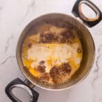Adding butter to caramel sauce in a pot.