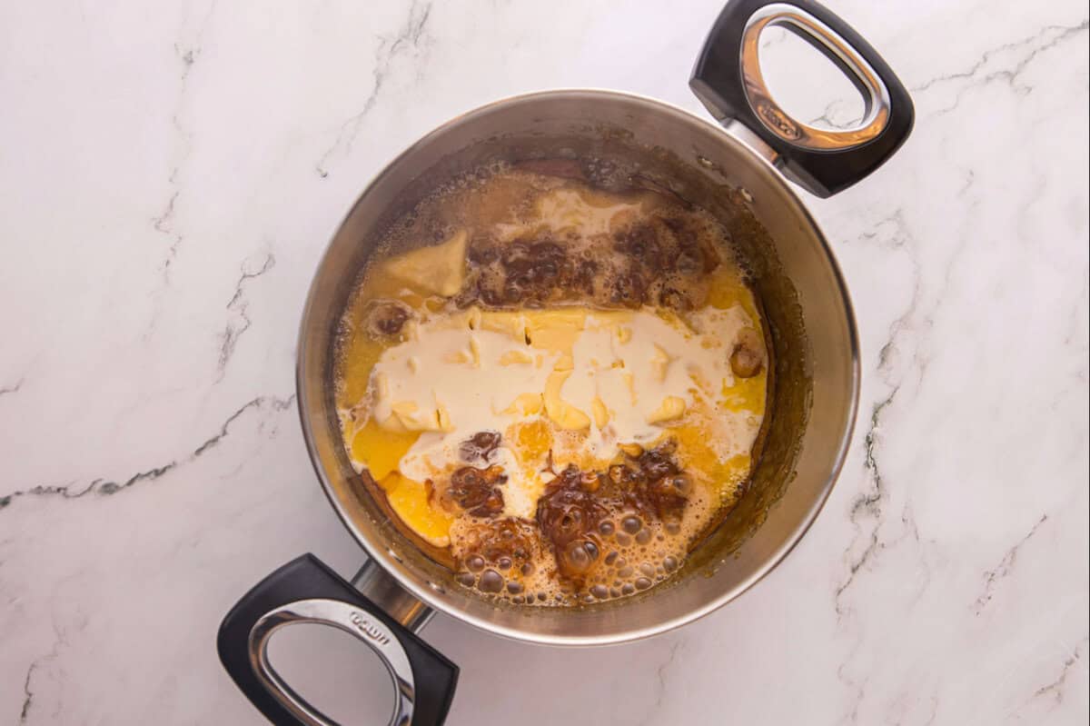 Adding butter to caramel sauce in a pot.