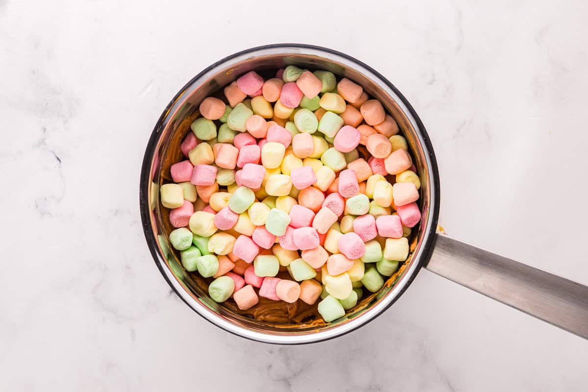 Rainbow marshmallows added to a saucepan with peanut butter mixture.