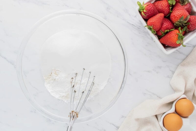 Whisking dry ingredients together in a glass mixing bowl.