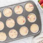 Strawberry-filled muffin batter in a muffin tin.