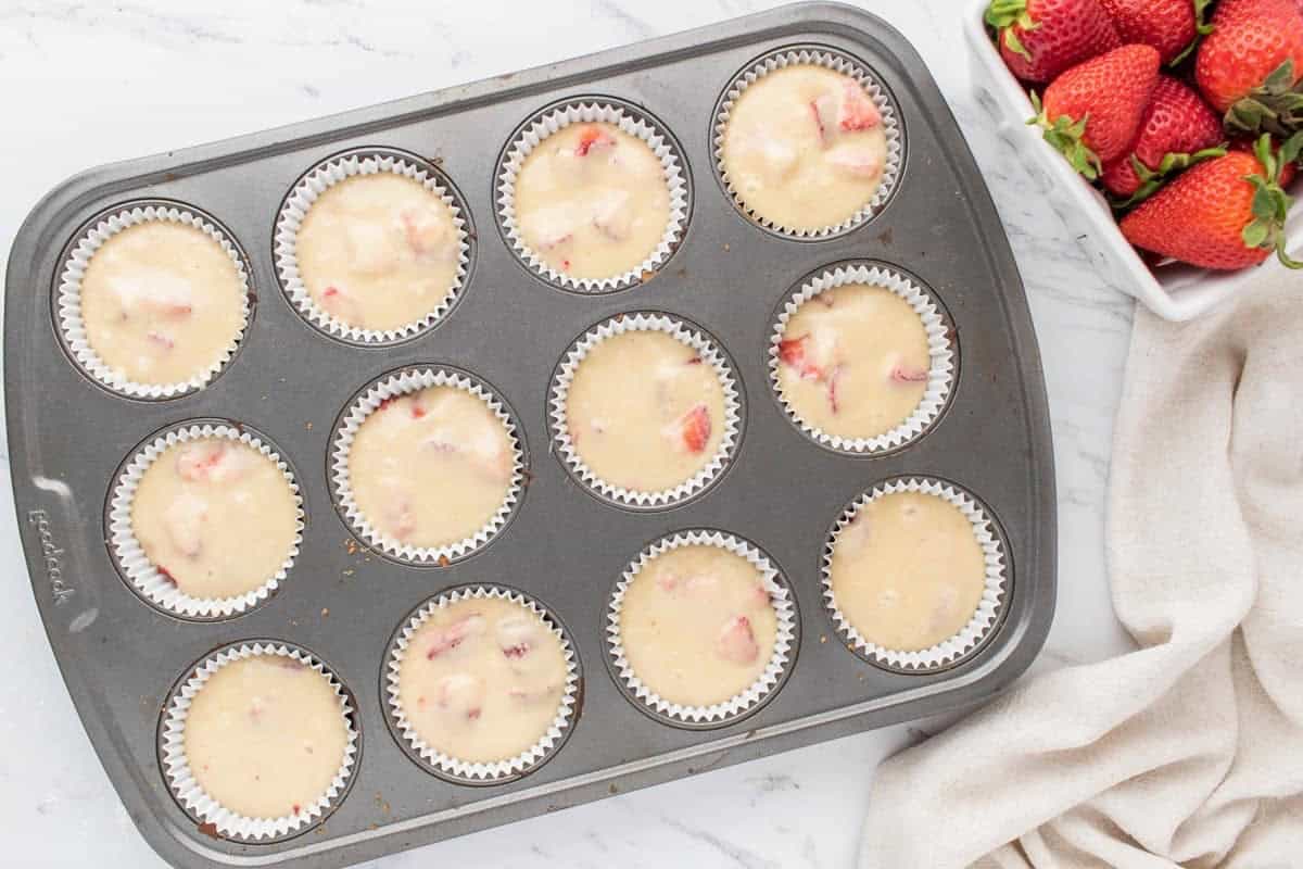 Strawberry-filled muffin batter in a muffin tin.