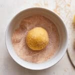 A snickerdoodle dough ball in a bowl of cinnamon sugar.