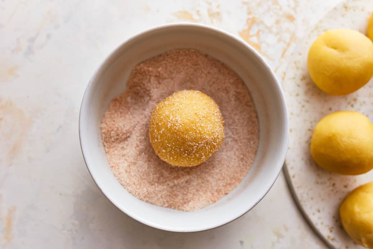 A snickerdoodle dough ball in a bowl of cinnamon sugar.