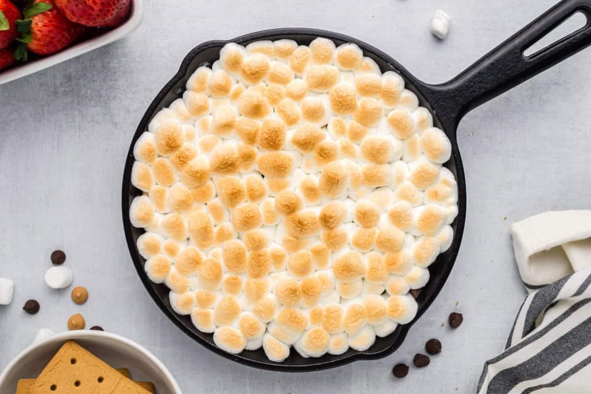 Baked s'mores dip in a cast iron skillet with browned marshmallow topping.