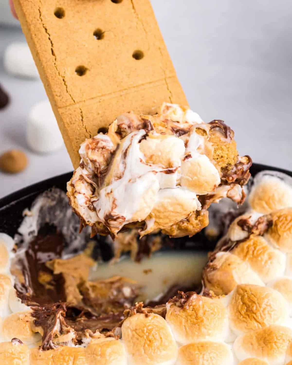 Graham cracker dipping into skillet s'mores dip.