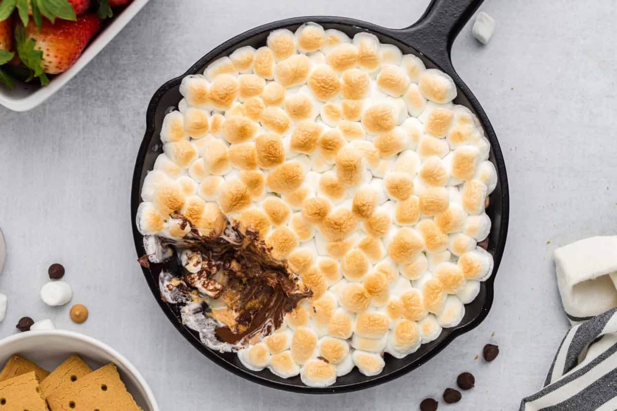 Skillet s'mores dip with a bite taken out, revealing the melted chocolate inside.