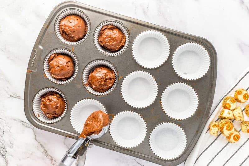 Spooning chocolate batter into cupcake tin.
